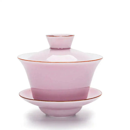A delicate pink ceramic gaiwan with gold trim paired with a celadon tea tureen in a light blue tea set