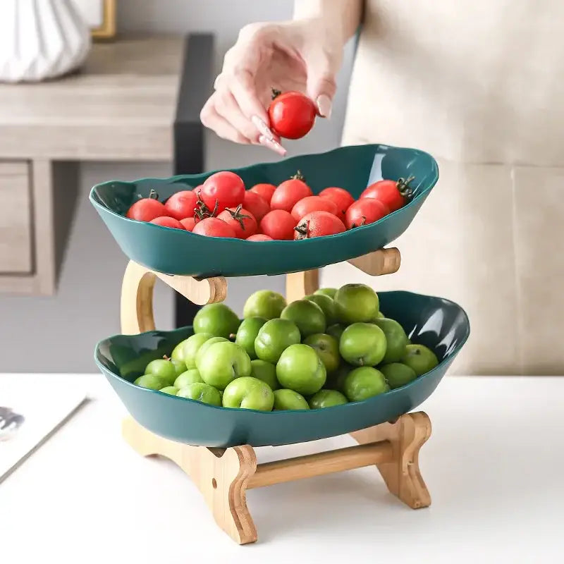 Teal ceramic two-tier fruit stand with wooden legs and curved bowls as part of a ceramic table plates set
