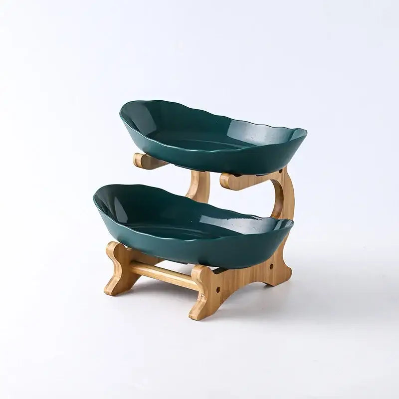 Two-tiered ceramic table plates set with leaf-shaped teal bowls on a light wood stand for dining room use
