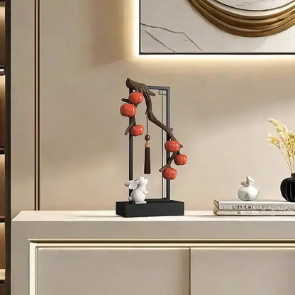 A sleek black metal stand with a curved branch holding glossy red ceramic persimmon and a white ceramic rabbit for living room home decor set