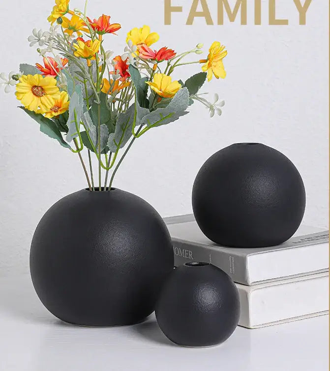 Ceramic round vase black white with black matte finish and one vase holding artificial yellow and orange flowers