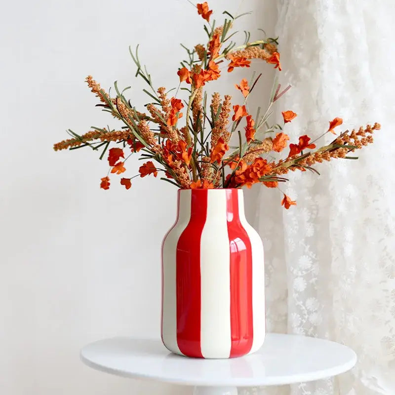 A glossy red striped ceramic vase with white vertical stripes holding orange flowers