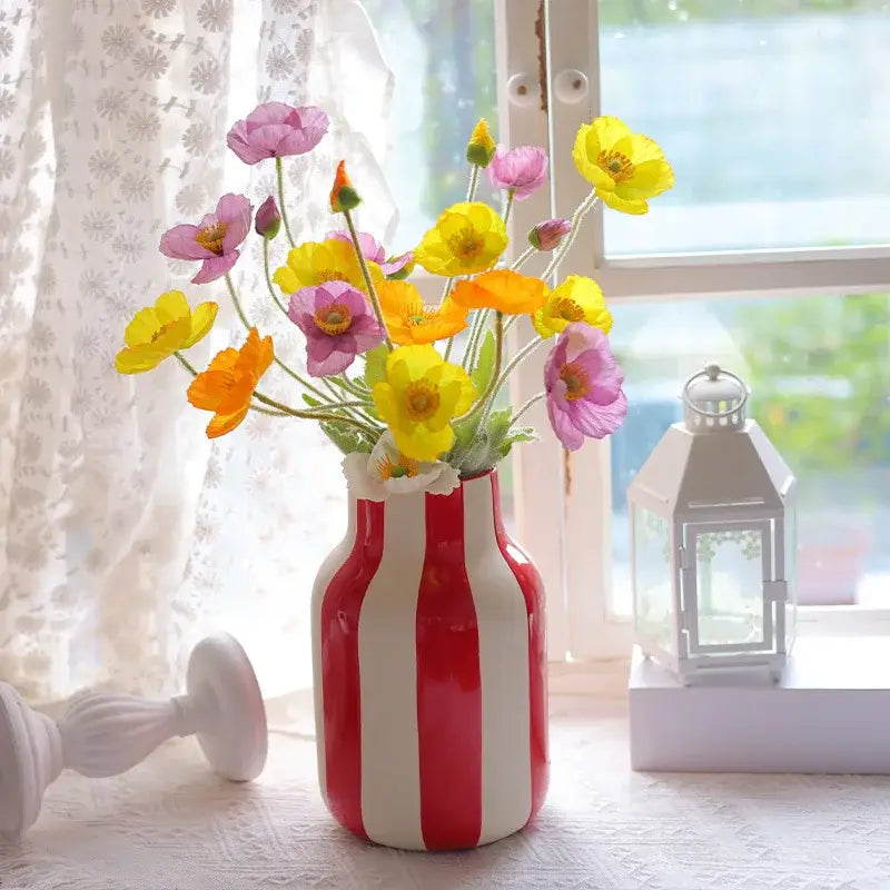 Ceramic vase black red striped with vibrant red and white vertical stripes holding a bouquet of colorful artificial poppies