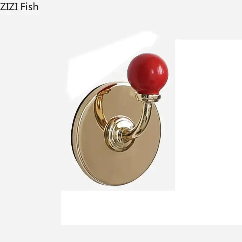 A polished gold-toned wall hook with a glossy red ceramic sphere for decorbites colorful wall storage organizer