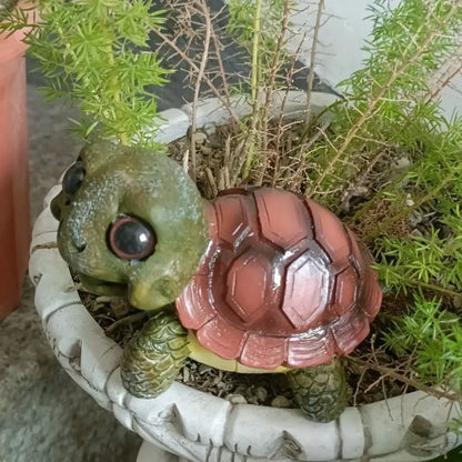 A charming green and reddish-brown plastic crawling turtle sculpture with glossy eyes in a white planter for decorbites crawling turtle decor