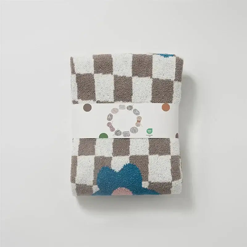 A soft plush beige and white checkered decorbites knitted blanket throw 130x160cm with blue floral design at bottom