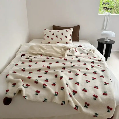 Cream-colored rollie loop fleece blanket with red cherry embroidery green stems and pom-poms on corners sheep rollie loop