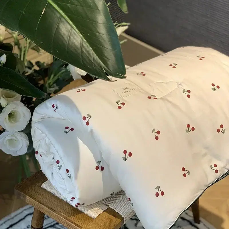 A soft off-white decorbites cooling quilt with red cherry embroidery and green stems for bedroom use