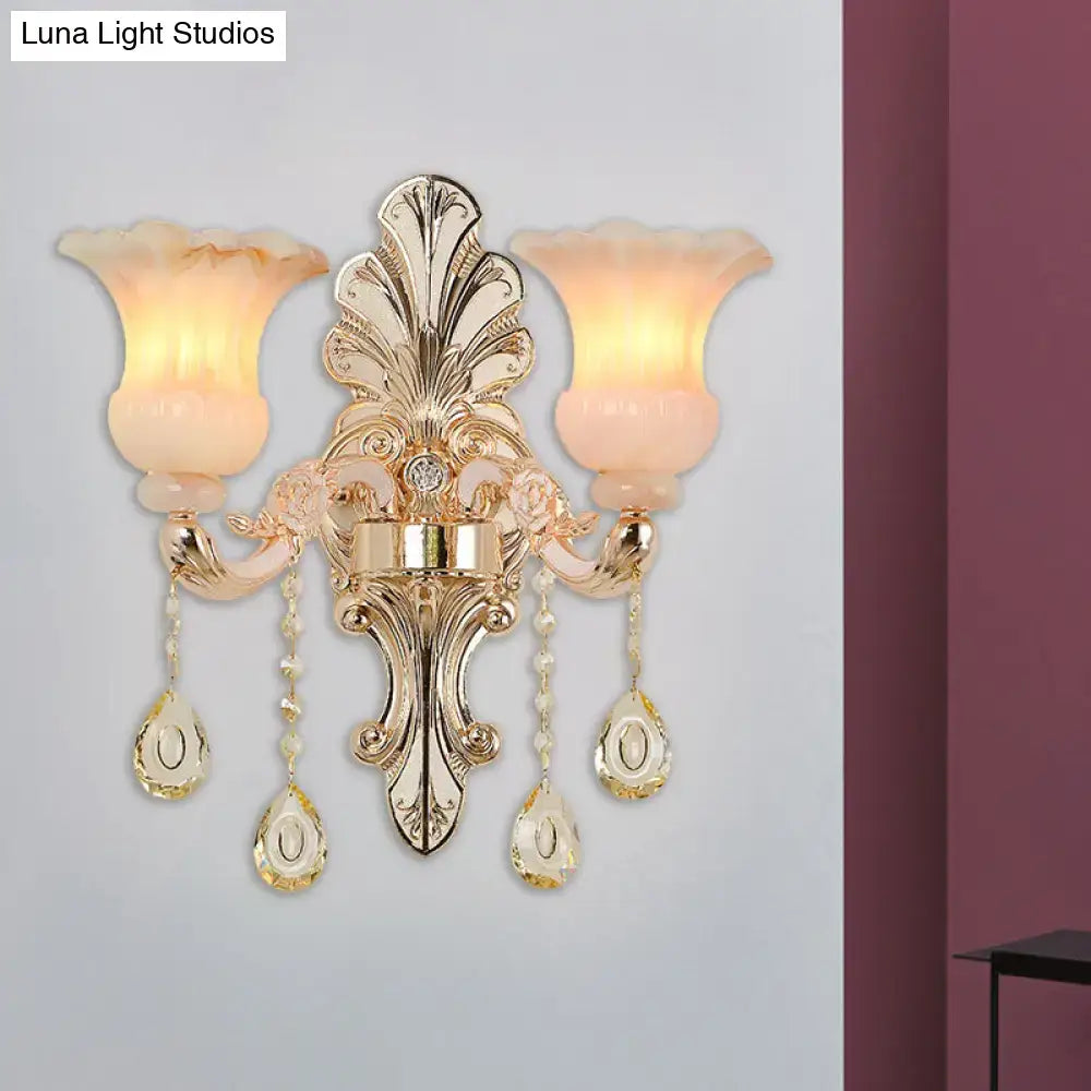 Gold-toned ornate wall lamp with two frosted peach glass shades and pink crystal teardrop pendants for bedroom use