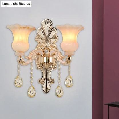 Gold-toned ornate wall lamp with two frosted peach glass shades and pink crystal teardrop pendants for bedroom use
