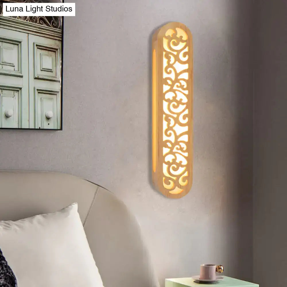 A warm golden beige carved wood wall light fixture with elongated oval shape and intricate scrollwork design
