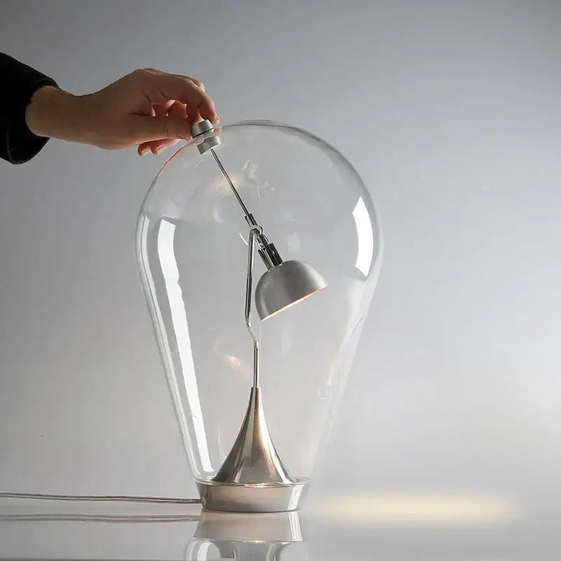 A sleek led table lamp with a transparent glass dome, polished chrome curved arm, and black shade for bedroom use