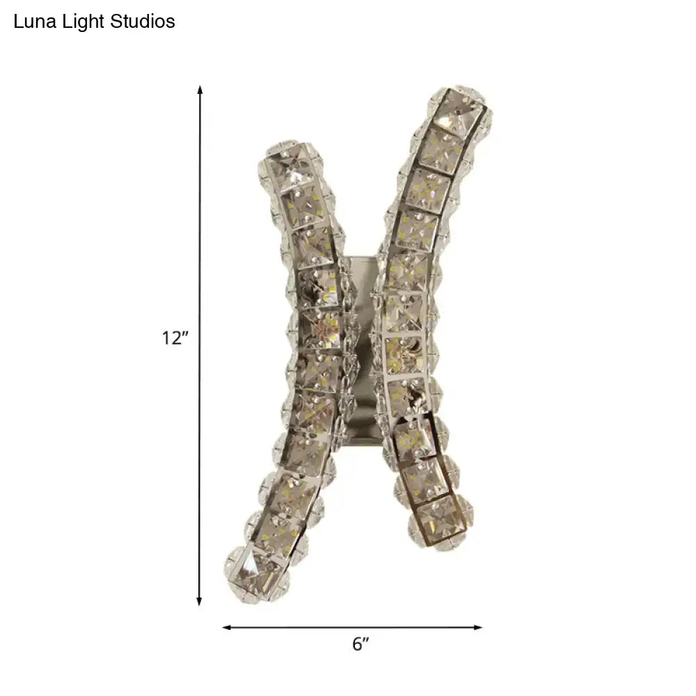 A chrome curvy wall sconce featuring a sparkling silver x shape with rows of clear crystal prisms for living room use