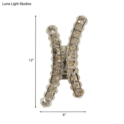 A chrome curvy wall sconce featuring a sparkling silver x shape with rows of clear crystal prisms for living room use