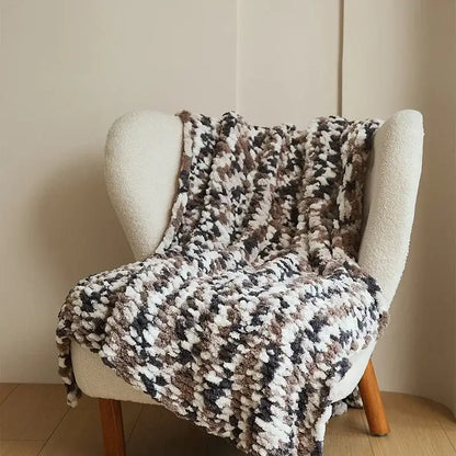 A cozy chunky knit jacquard blanket throw in white beige and dark brown draped over a cream armchair