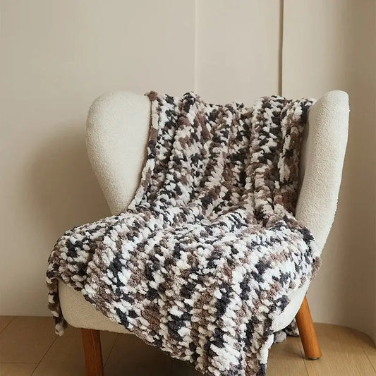 A cozy chunky knit jacquard blanket throw in white beige and dark brown draped over a cream armchair