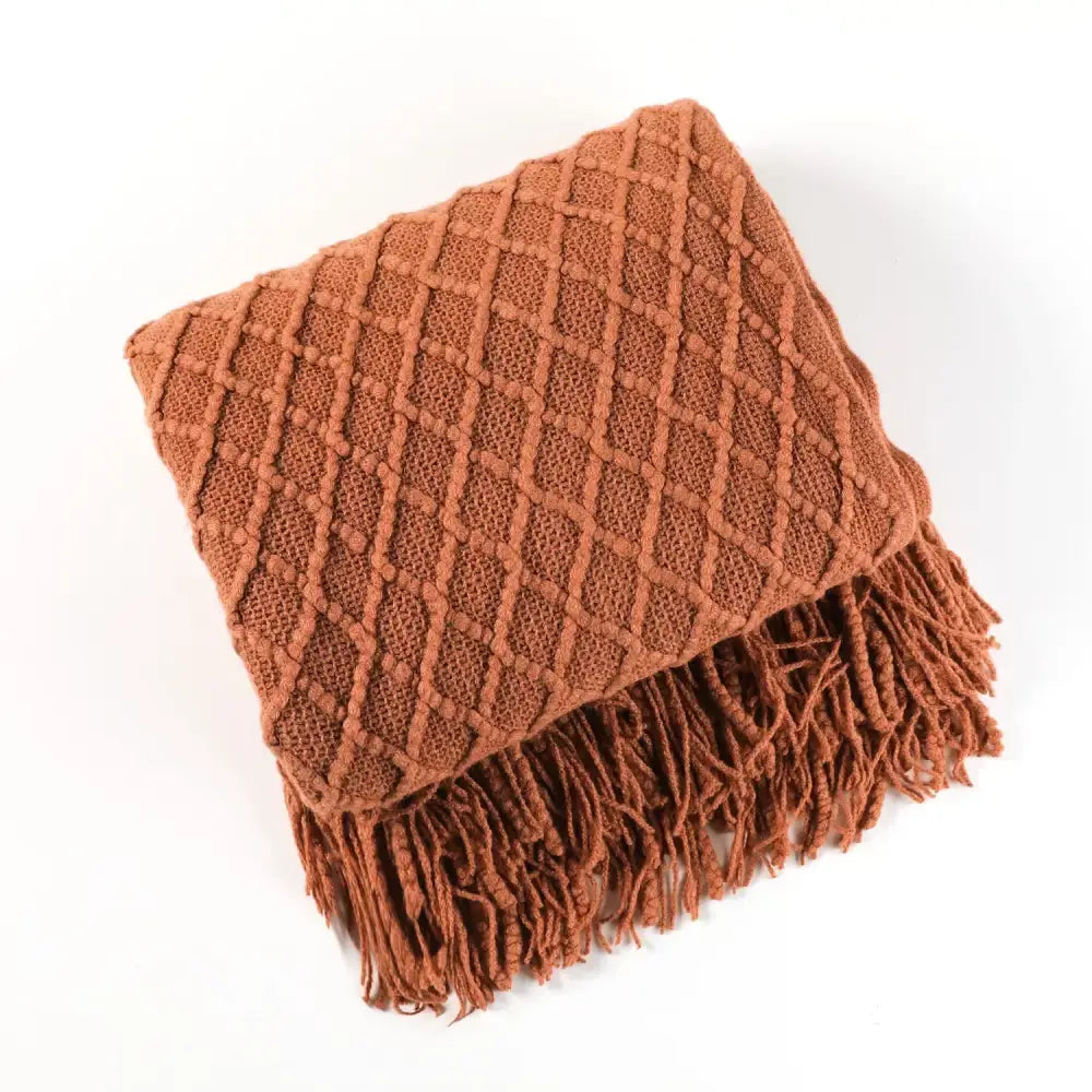 A cozy knitted sofa blanket in terracotta with a diamond pattern and fringed edges for living room comfort