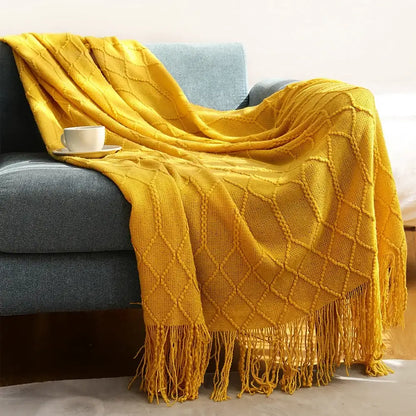 A cozy knitted sofa blanket in mustard yellow with a chunky ribbed diamond pattern and fringe for living room comfort