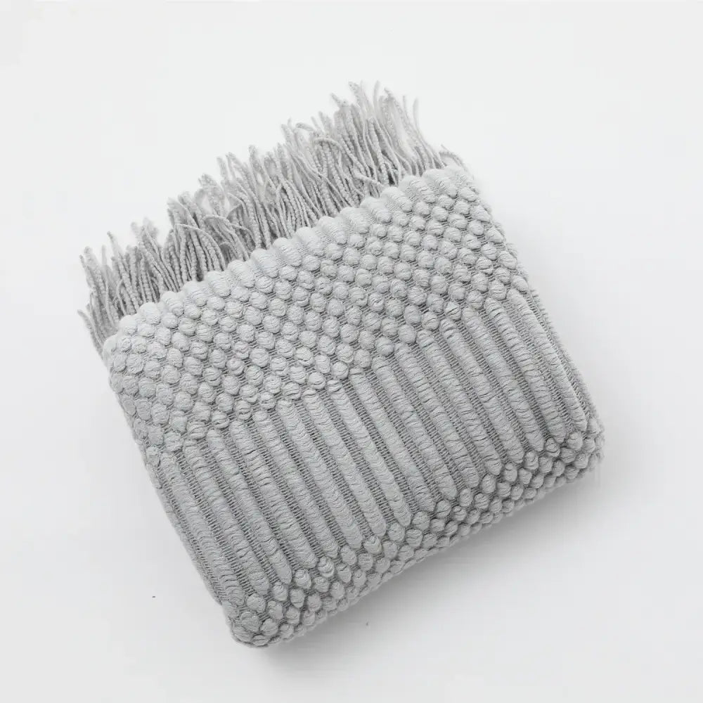 A soft light gray cozy knitted sofa blanket with raised dot texture and fringed edges for living room decorbites comfort
