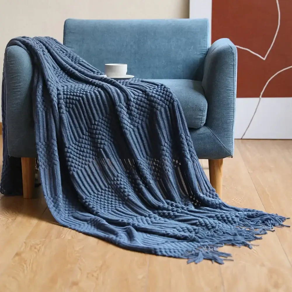 A cozy knitted sofa blanket in navy blue macrame with textured woven pattern and fringed edges for living room comfort
