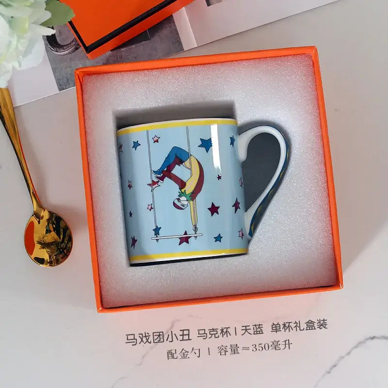 A light blue ceramic mug with a yellow rim featuring a colorful acrobat illustration from decorbites circus troup kids tableware set