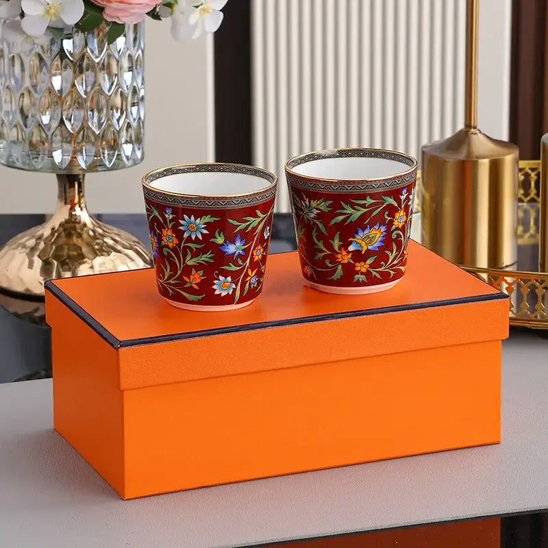 Two matching red ceramic cups with floral patterns and gold rims from decorbites circus troup kids tableware set