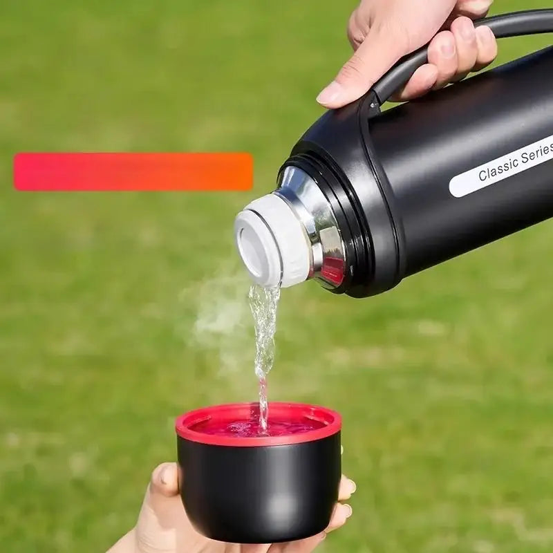 Classic black and red vacuum thermos flask pouring steaming water into matching cup for outdoor use