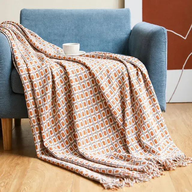 A cozy, textured throw blanket with a geometric pattern of orange and gray squares draped over a blue armchair.