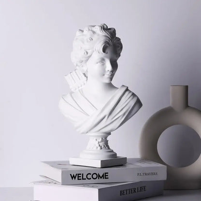 Classical white cupid statue plaster sculpture with curly hair and draped fabric resting on stack of books for decor