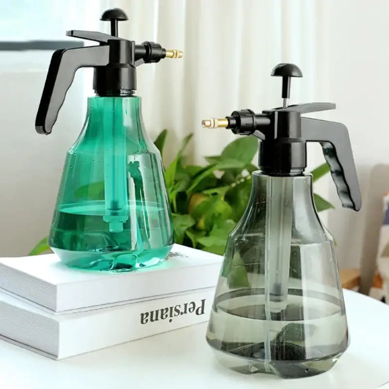 Two transparent plastic hand trigger watering sprayers with black handles and brass nozzles, one with green liquid and one clear
