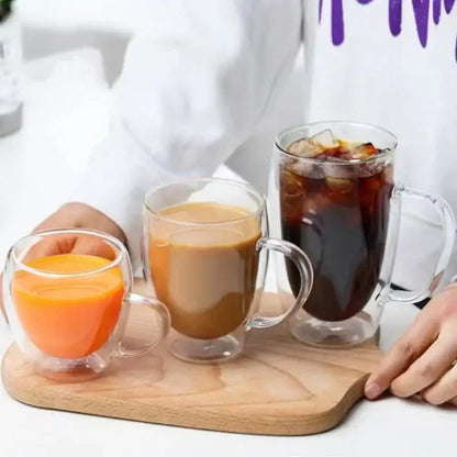 Three clear double wall high borosilicate glass mugs filled with orange juice latte and iced coffee on wooden board