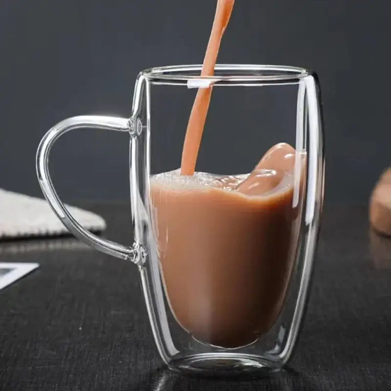 A clear double wall high borosilicate glass mug with handle filled with brown coffee topped with foam