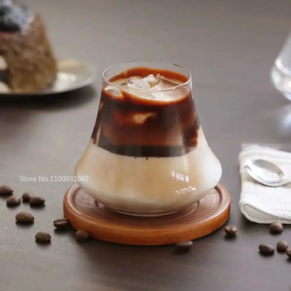 A clear glass cold brew latte drinkware set with wooden coaster featuring a layered iced coffee in a glass tumbler