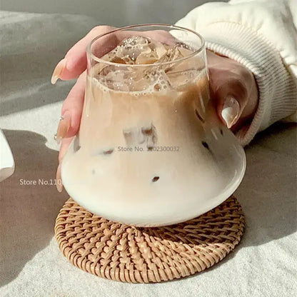 Clear glass cold brew latte drinkware set with wooden coaster featuring a tumbler filled with iced coffee on a rattan coaster