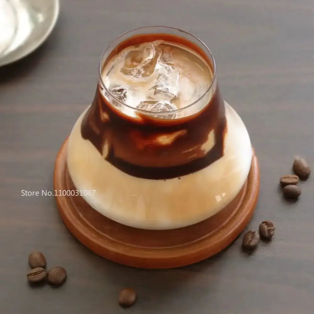 A clear glass cold brew latte drinkware set with swirling brown and creamy white layers on a wooden coaster