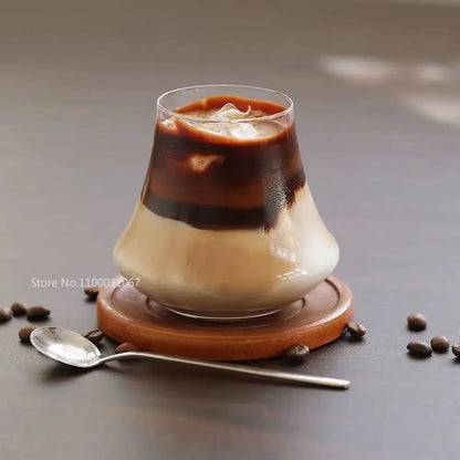 A clear glass cold brew latte tumbler in a drinkware set resting on a wooden coaster for brew latte whiskey use