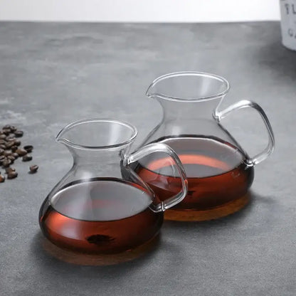 Two clear glass drip pot coffee carafes with curved handles filled with amber liquid in a pot coffee set