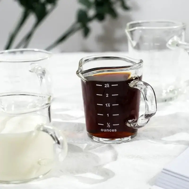 Clear glass espresso measuring cup with handle filled with dark liquid marked in ounces for precise measuring