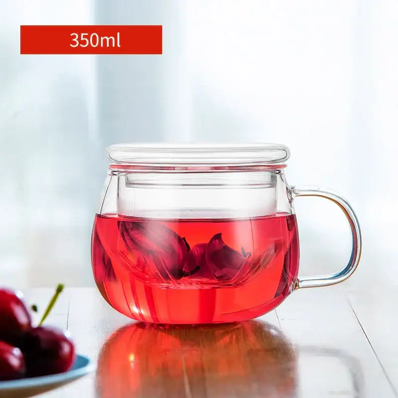 Clear glass floral tea cup with lid and handle filled with vibrant red hibiscus floral tea in kitchen teaware