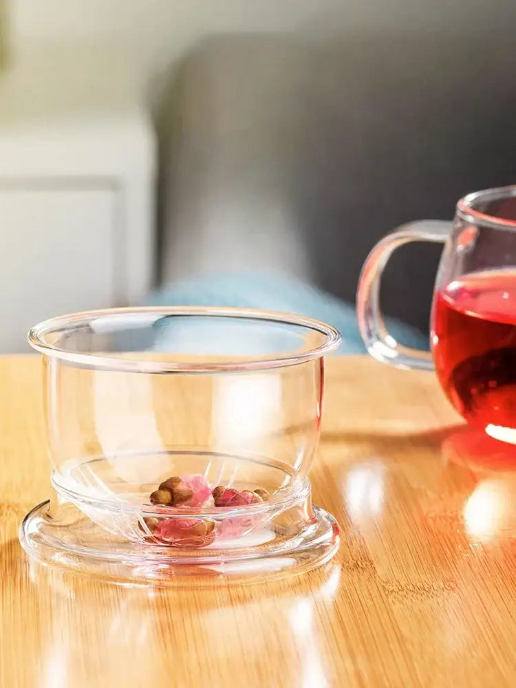 Clear glass floral tea cup with matching saucer containing dried pink and brown herbs for floral tea brewing