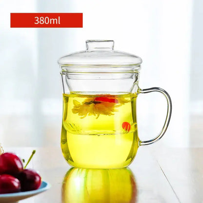 Clear glass floral tea cup with lid and handle filled with yellow tea and floating flower petals for teaware use