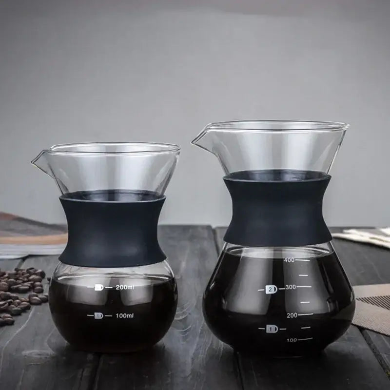 Two clear glass pour over coffee makers with black silicone bands and stainless steel filters filled with brewed coffee