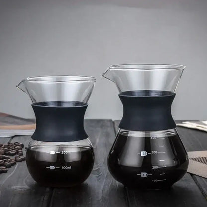 Two clear glass pour over coffee makers with black silicone bands and stainless steel filters filled with brewed coffee