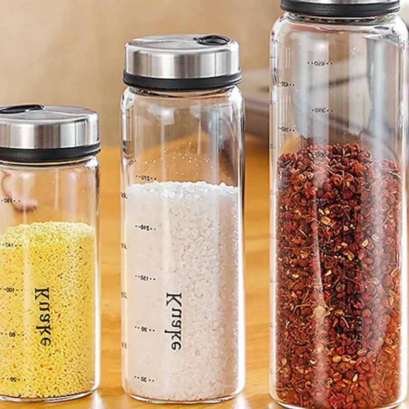 Three clear glass spice shaker jars with rotary lids and stainless steel tops labeled kuske for salt sesame pepper storage