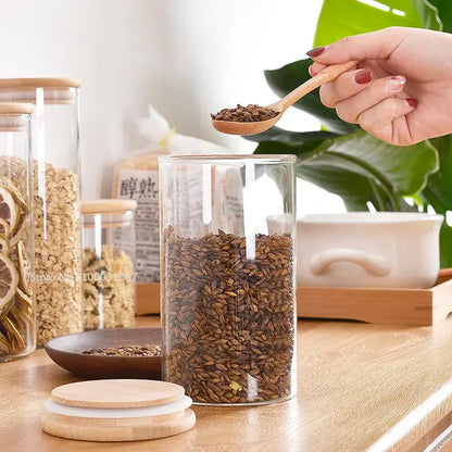 Clear glass storage jar with bamboo lid and wooden spoon filled with brown grains for kitchen organization