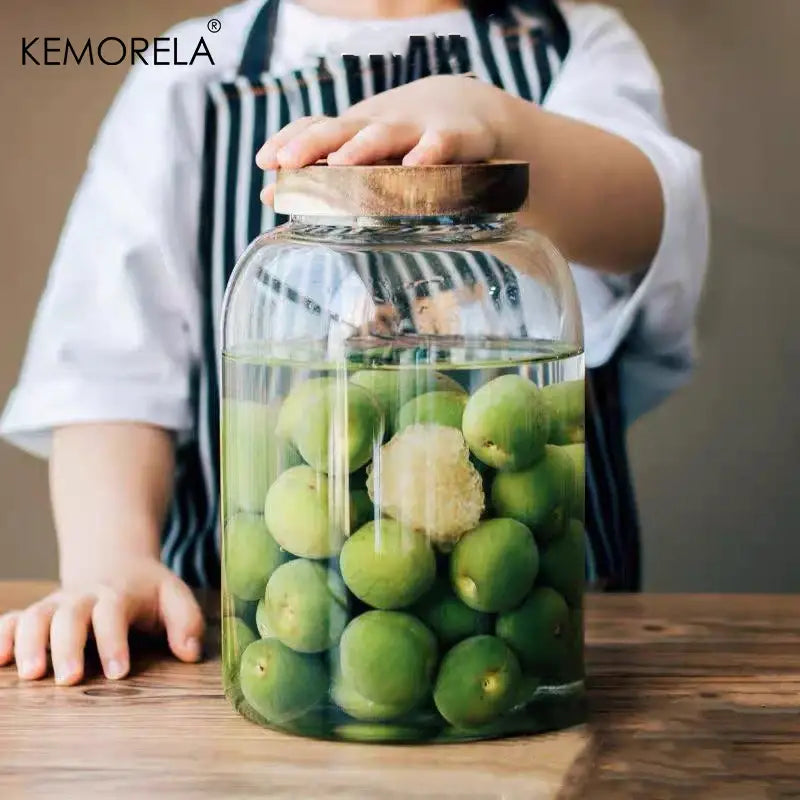 Clear kitchen glass jars with acacia lids filled with green plums and ginger for food storage use
