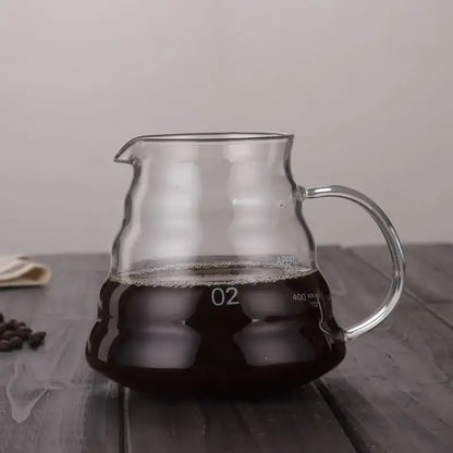 Clear glass cloud shaped glass coffee kettle with curved handle filled with dark brewed coffee by decorbites