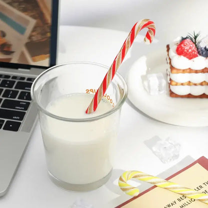 A colorful christmas long handle candy cane glass stirring stick in red and gold stripes in a clear glass of milk