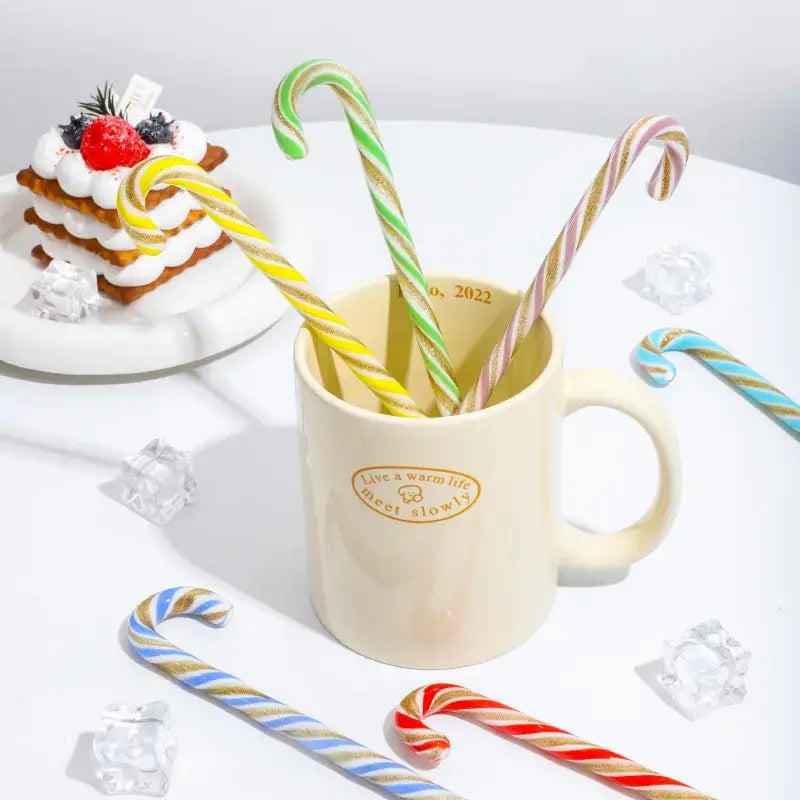 Cream-colored ceramic mug with gold foil stamping holding colorful christmas long handle striped candy canes decorbites colorful christmas