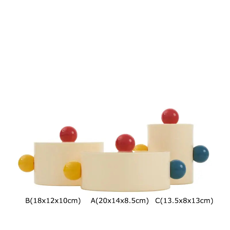 Cream-colored cylindrical ceramic storage jar with colorful dot decorative spheres in red yellow and blue for bedroom organization